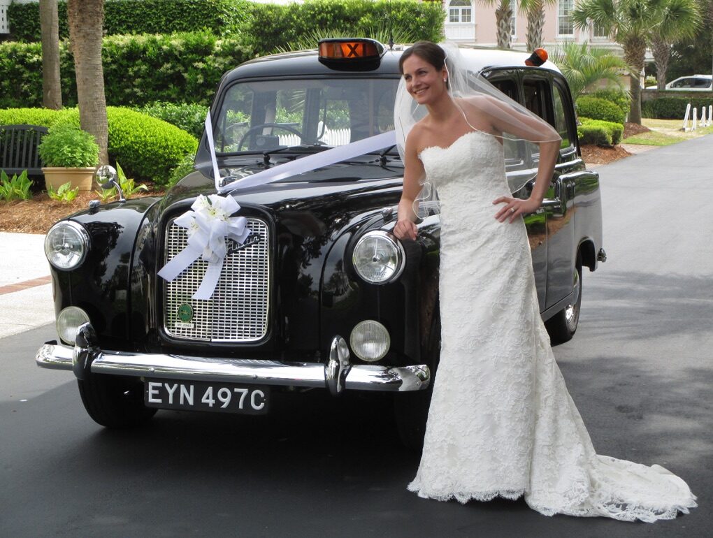 A bride leaning against the front wing of the black 1965 Austin FX4 taxi, white ribbon and a spray of flowers tied to the radiator grille.